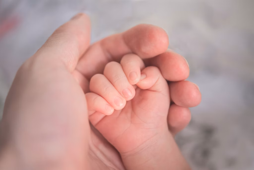 Close-up little hand of child baby holding hand of mother, A newborn holds on to mom'
